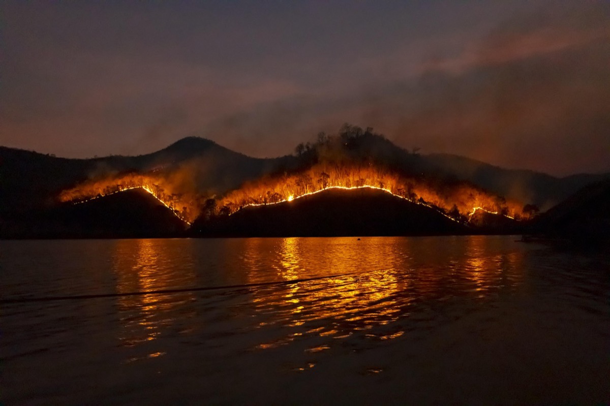 Active wildfire with smoke rising over water and landscape